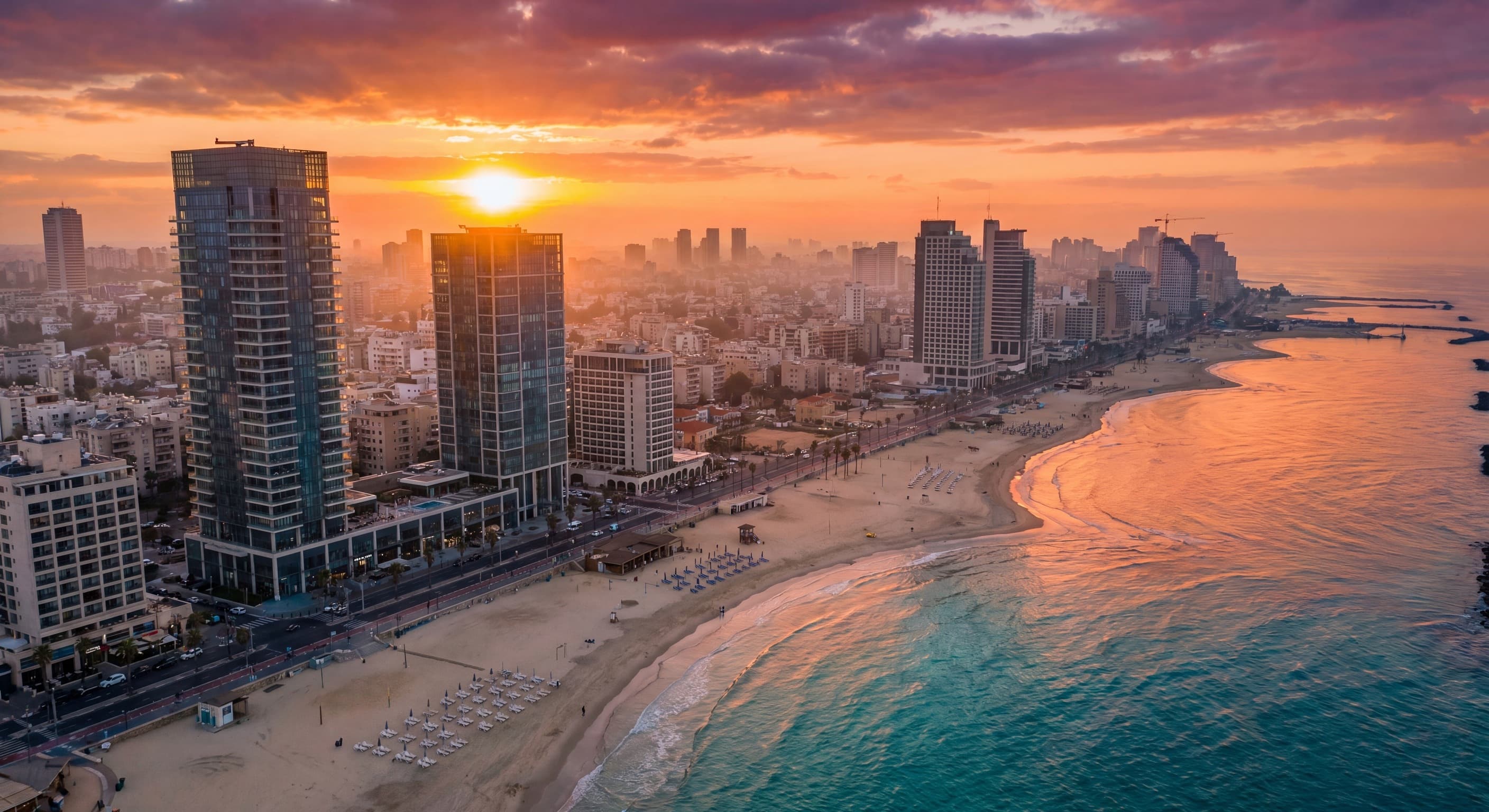 מבט אווירי על קו החוף של תל אביב עם חוף ומגדלים בשקיעה זהובה — תמונת נושא לתושבים חוזרים ועולים חדשים
